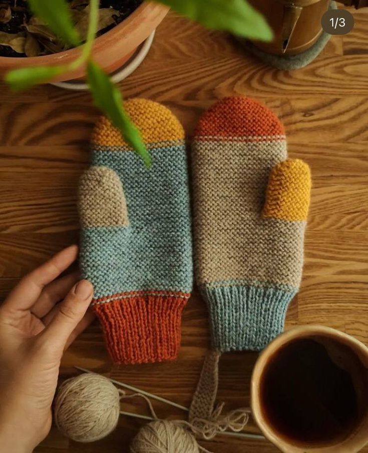 two knitted mittens sitting on top of a wooden table next to a cup of coffee