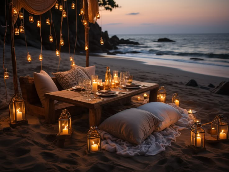 a table set up with candles and pillows on the beach