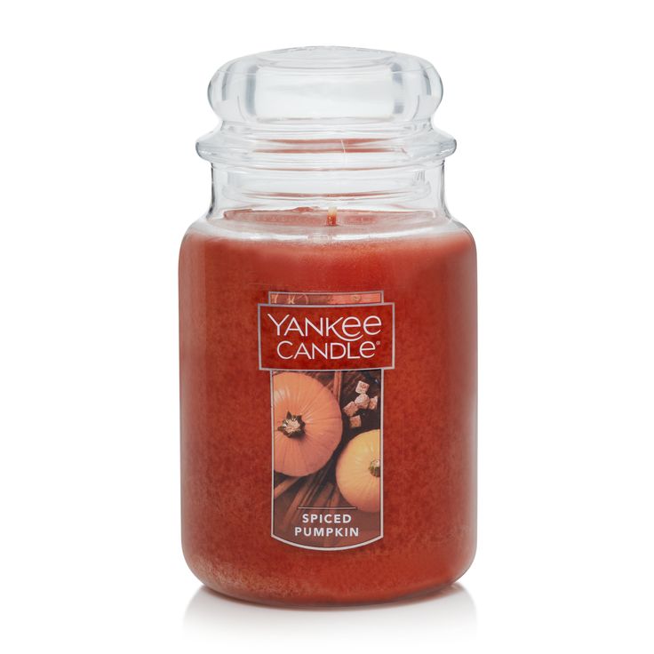 a large jar filled with an orange colored candle next to a white background and the words yankee candle written on it