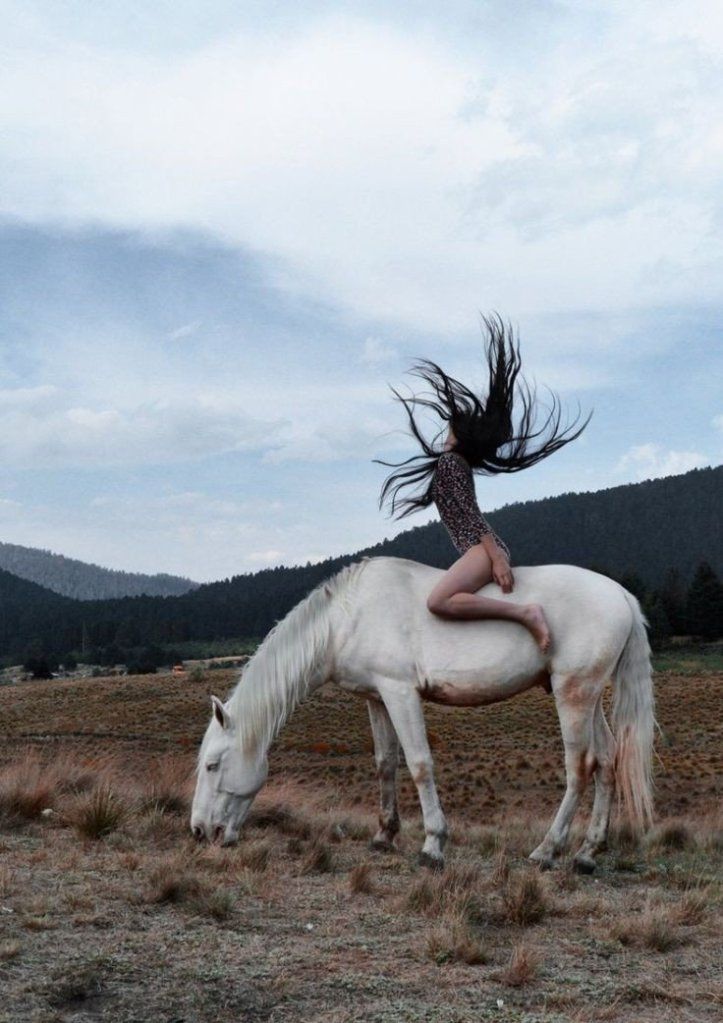 a woman riding on the back of a white horse in a dry grass covered field