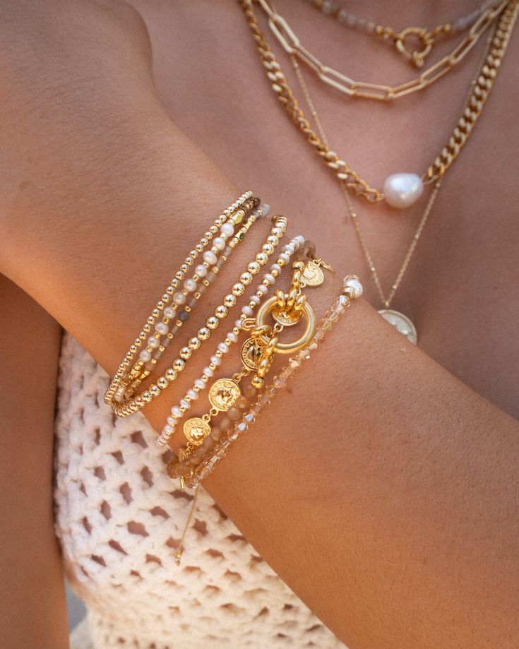 Your new favorite stacking bracelet. Featuring genuine champagne gold Swarovski crystal beads with gold and freshwater pearl accents, this bracelet sparkles at every angle, no filter needed. The champagne tone pairs well with gold, so layer a few up with our OG gold bracelets. Champagne Swarovski crystals Freshwater Pearl and 14k Gold Fill components Elastic bracelet Dimensions: Fits 5.75"-6.9" wrist Please avoid exposing freshwater pearls to perfumes or harsh chemicals Make your jewelry last! C Jewelry Stacking Ideas, Stackable Gold Bracelets, Golden Bracelet Stack, Cool Tone Jewelry, Bracelet Stack Inspo Gold, Bracket Stack Ideas, Gold Bracelet Stack Aesthetic, Swarovski Jewelry Gold, Gold Bracelet With Pearls