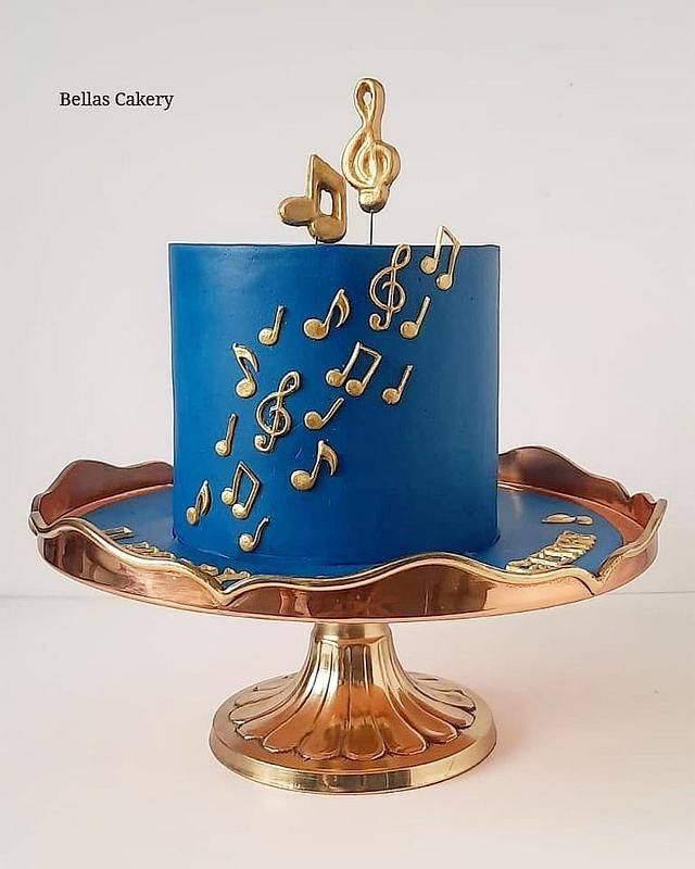 a blue and gold cake with musical notes on the top is sitting on a stand