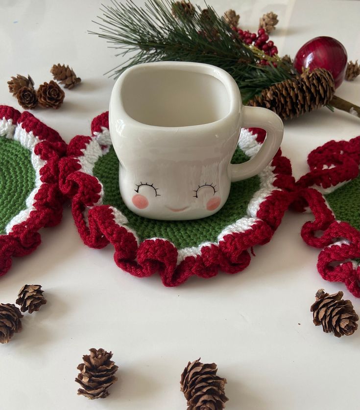 a coffee cup sitting on top of a crocheted place mat next to pine cones