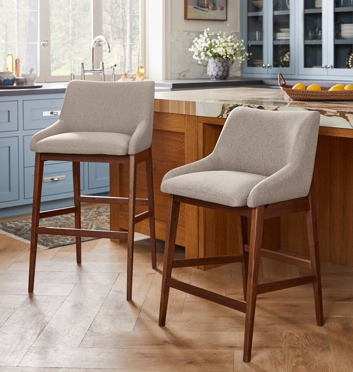 two stools in the middle of a kitchen with blue cabinets and counter tops on either side