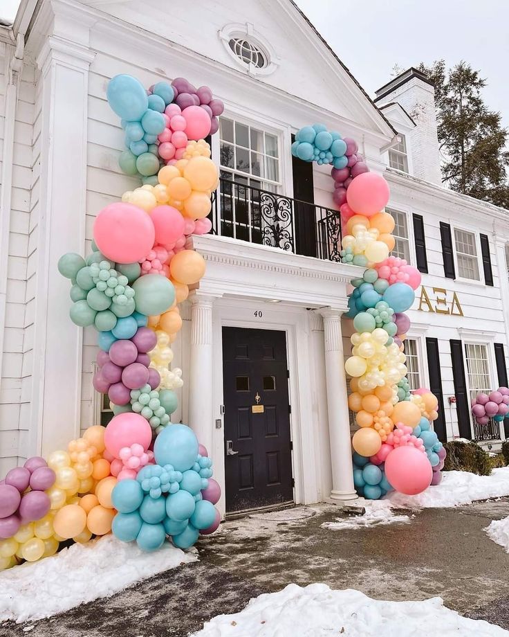 an arch made out of balloons in front of a white house with snow on the ground