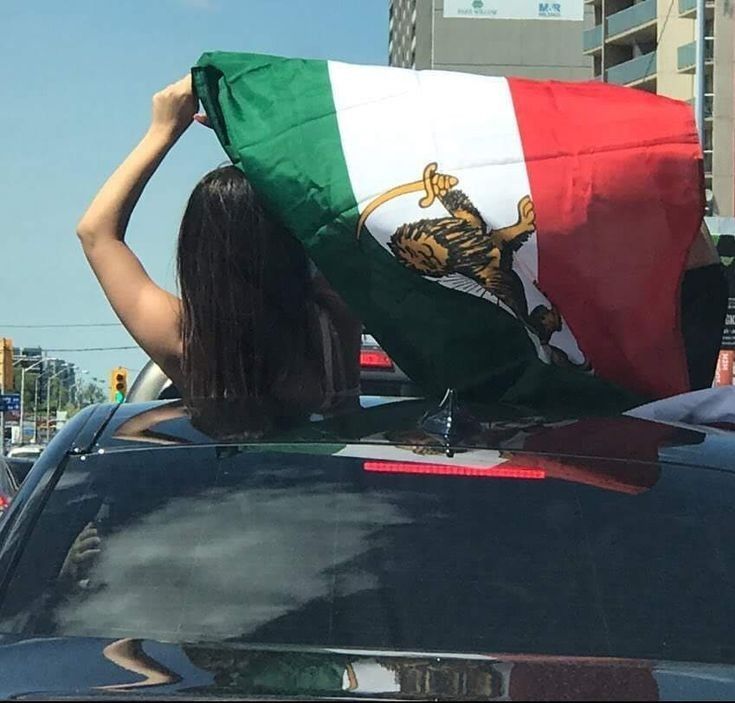 a woman holding a mexican flag in the back of a car