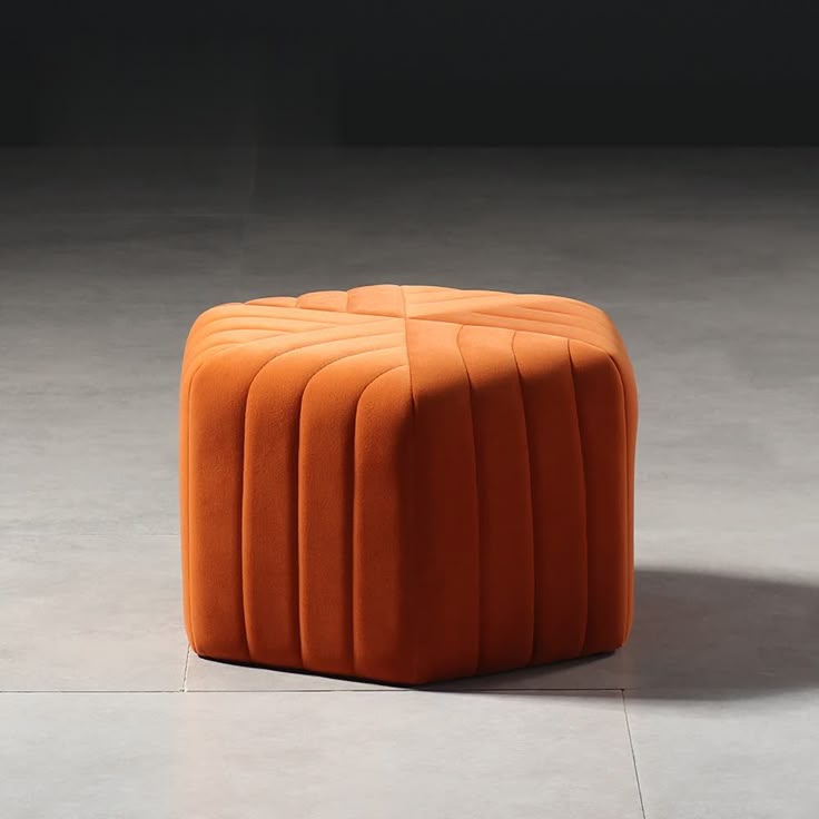 an orange ottoman sitting on top of a white floor next to a black wall with the words orange written above it