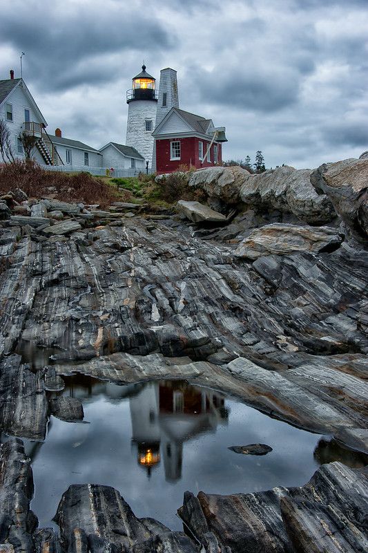 a lighthouse on top of a rocky hill next to a body of water with rocks in the foreground