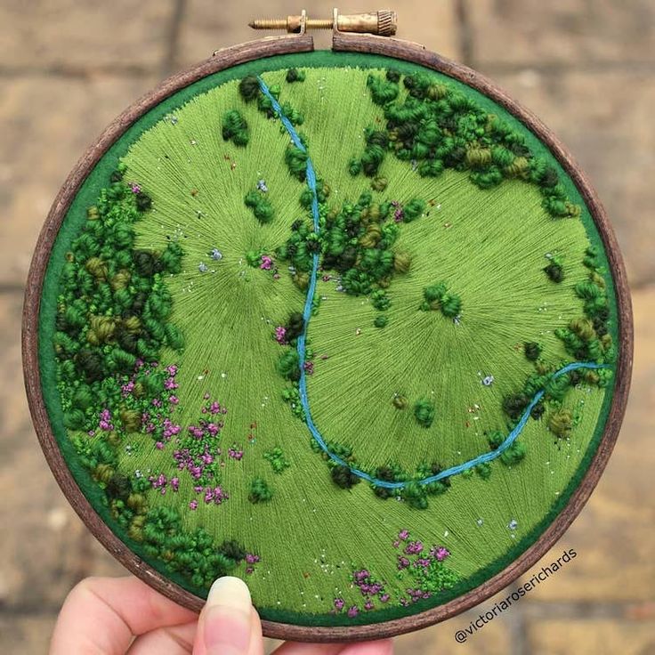 a person holding up a small embroidered patch with a river running through the middle of it