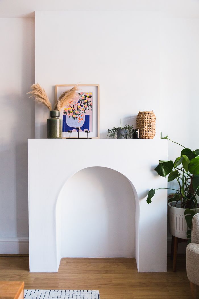 a living room with a white fireplace and potted plants