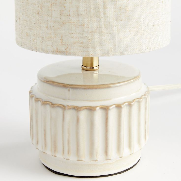 a white ceramic lamp with a beige shade on it's base and a gold plated metal light fixture