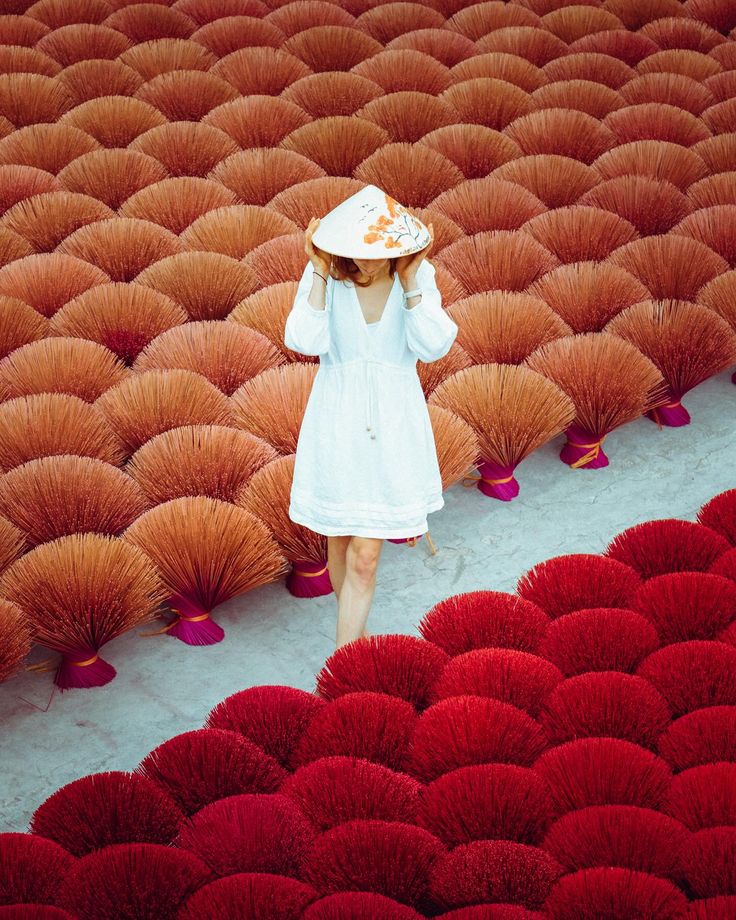 a woman in a white dress and straw hat walking through a field of red flowers