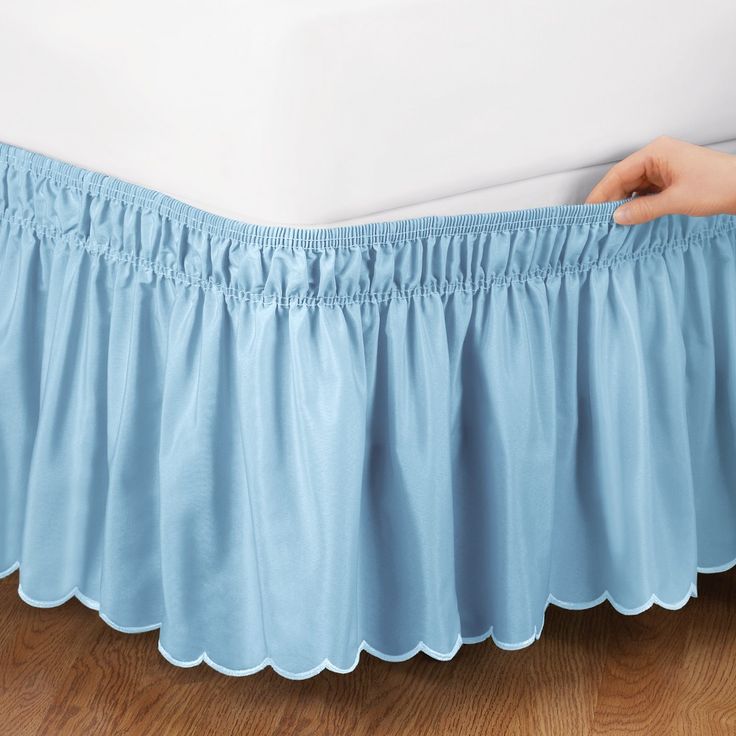 a person's hand is holding the edge of a bed with blue ruffled bedskirt