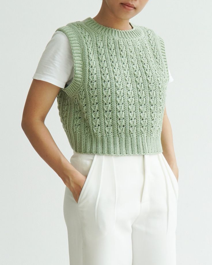 a woman is wearing a green knitted sweater and white pants with her hands on her hips