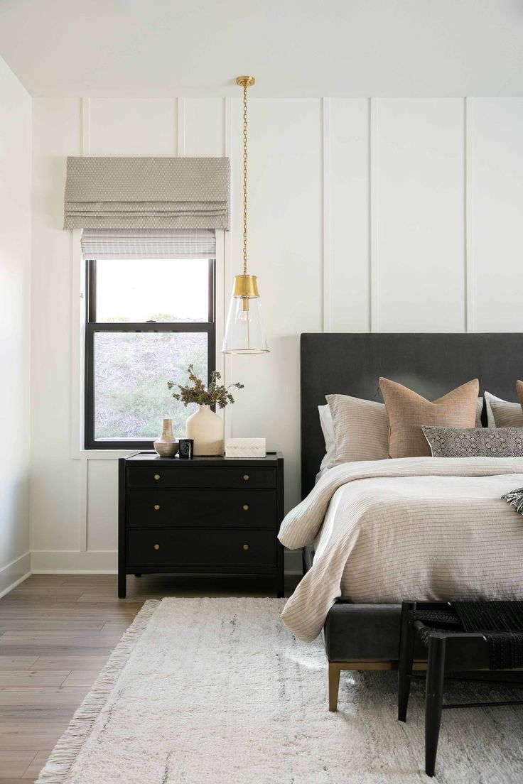 a bedroom with white walls and wood floors, black furniture, and a large window