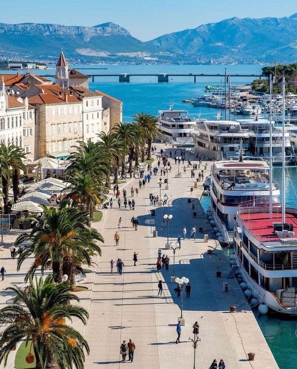 people are walking along the waterfront with boats in the water