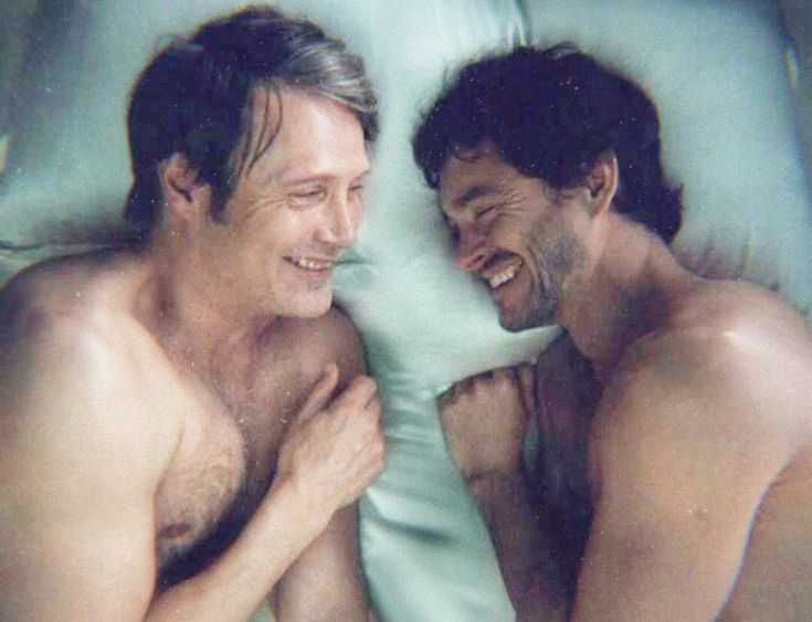 two men laughing while laying in bed together