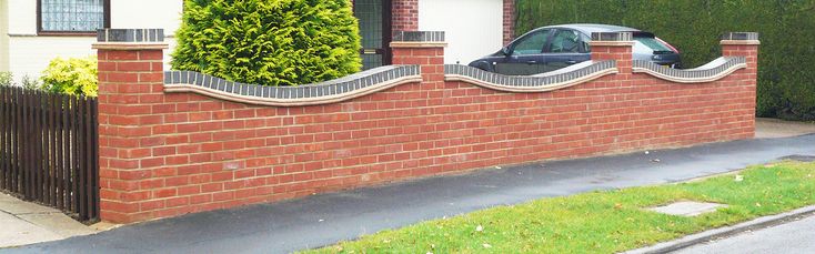 a car is parked in front of a brick wall and gated driveway area with green grass on both sides