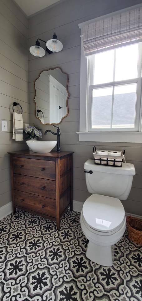 a white toilet sitting next to a wooden dresser in a bathroom on top of a black and white floor