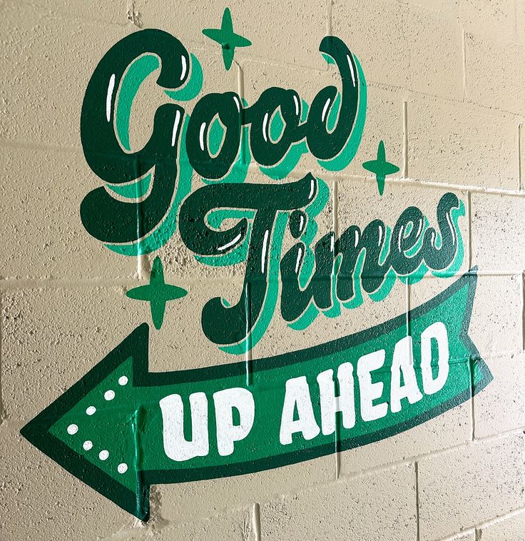 a painted sign that says good times up ahead on a brick wall with green arrows