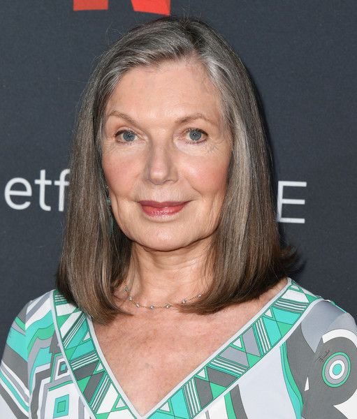 an older woman with grey hair and blue eyes smiles at the camera while standing in front of a black background