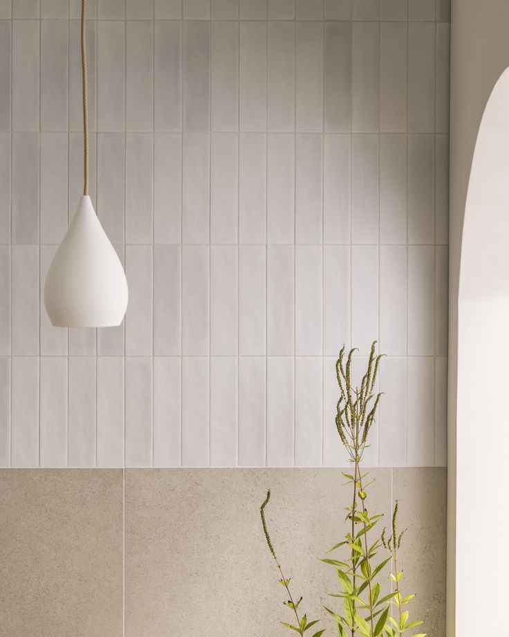 a plant in a vase next to a wall with tiles on it and a hanging light