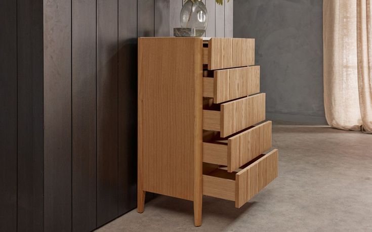 a tall wooden cabinet with five drawers and a vase filled with flowers sitting on top of it