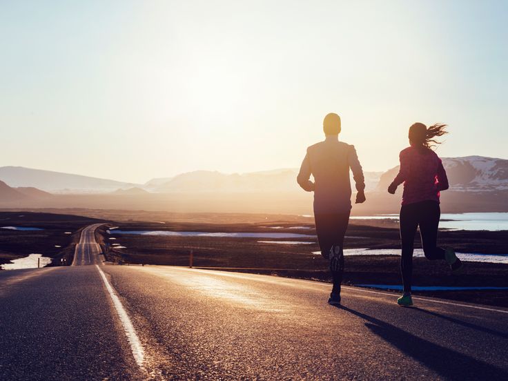 two people running down the road at sunset