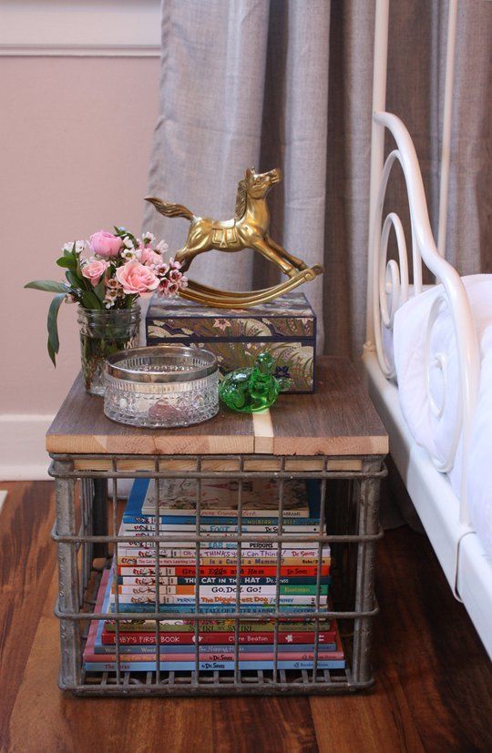 a small table with some books and flowers on it next to a metal bed frame