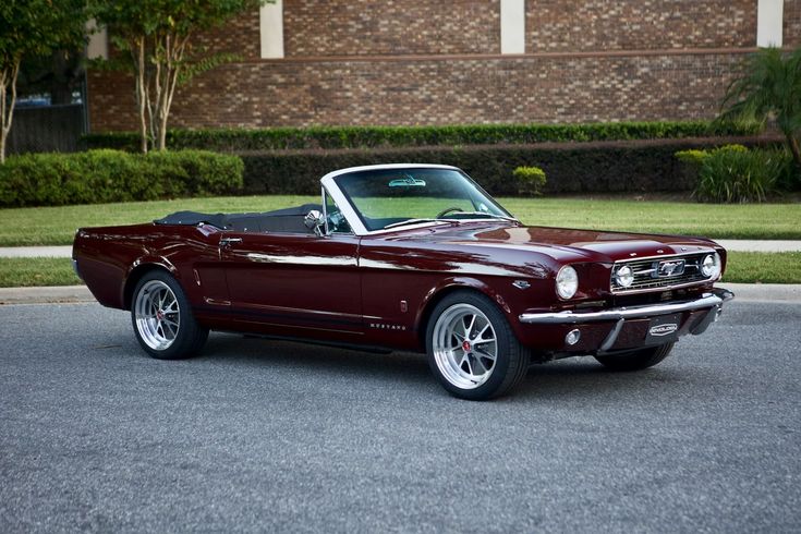 a maroon mustang parked in front of a brick building