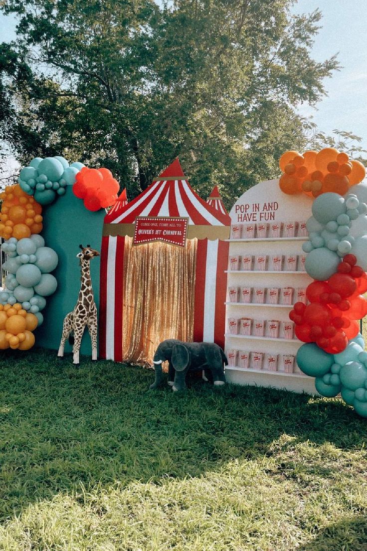 a circus tent with balloons and giraffes in the grass next to it