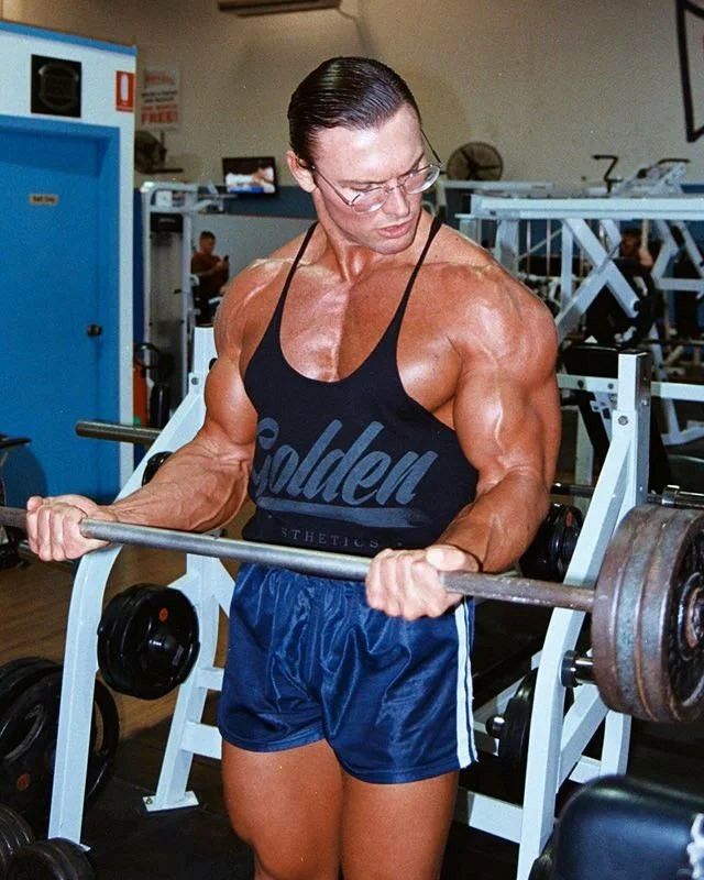 a man in shorts and tank top lifting a barbell with one hand on his hip