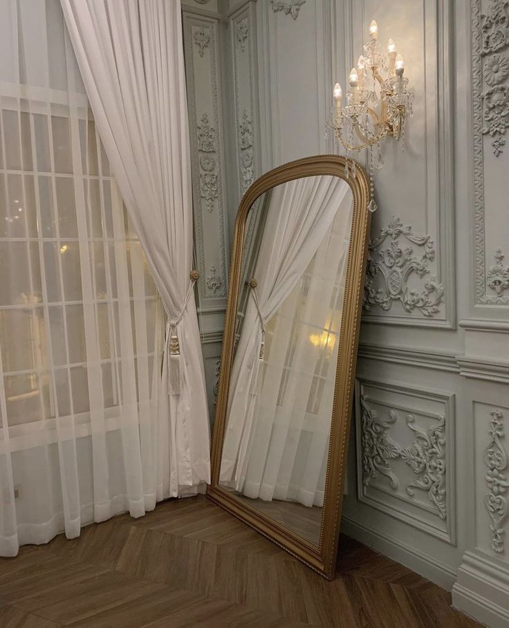 a large mirror sitting on top of a hard wood floor next to a white curtain