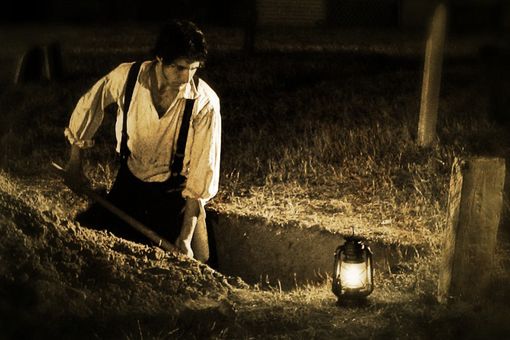 a man standing next to a lantern in the grass