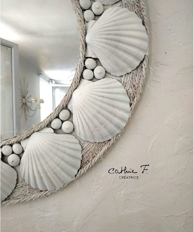 a mirror with seashells hanging on it's side next to a wall