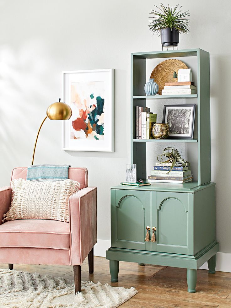 a living room with a pink chair and green bookcase next to a white wall