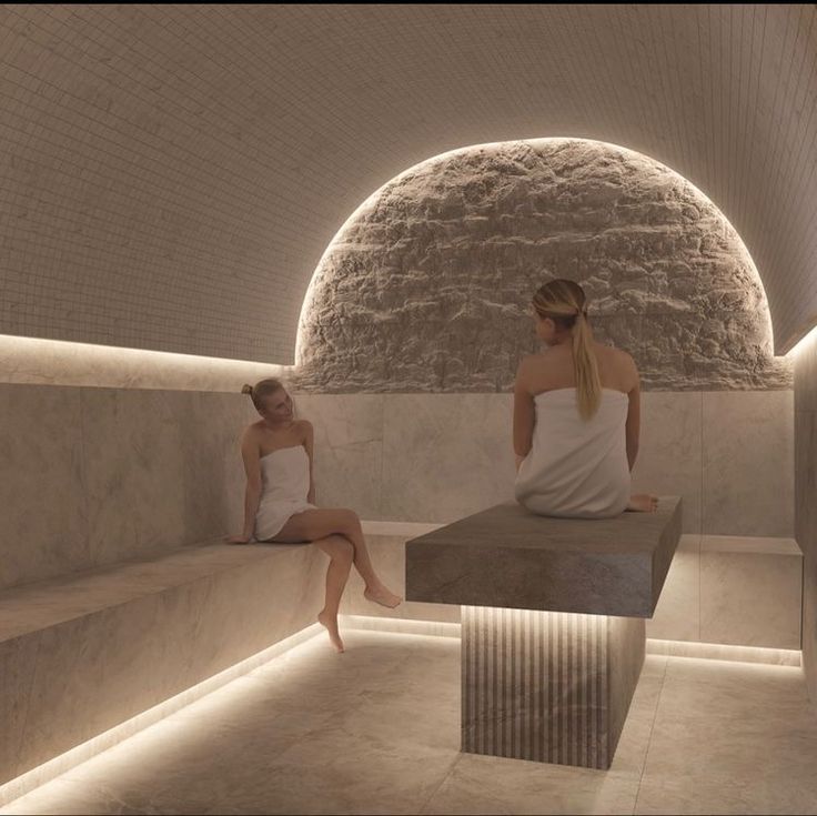 two women are sitting on benches in a room with stone walls and lights around them