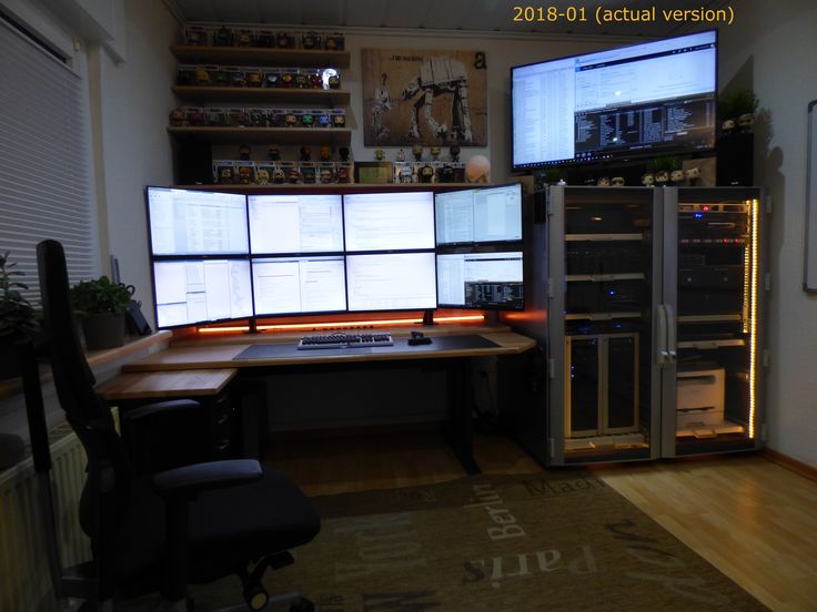 two computer screens sitting on top of a wooden desk in front of a wall mounted monitor