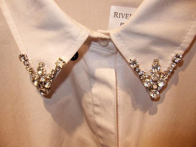 the collar of a white dress shirt with gold and crystal brooches on it