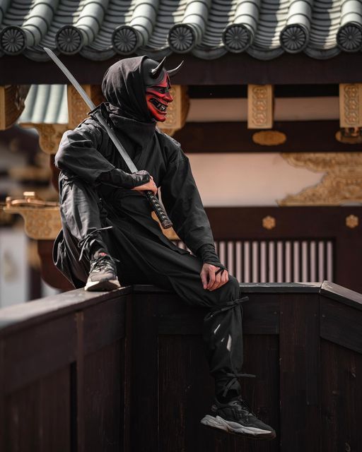 a man wearing a mask sitting on top of a wooden fence