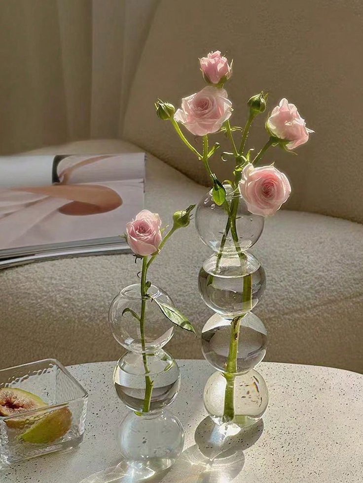 three clear vases with pink roses in them on a table next to a magazine