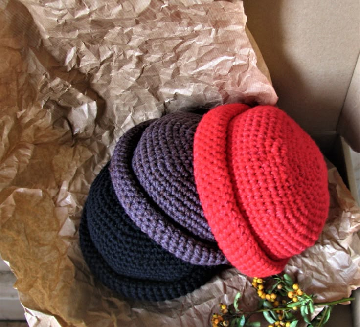 three knitted hats laying on top of each other in a pile of crumpled paper