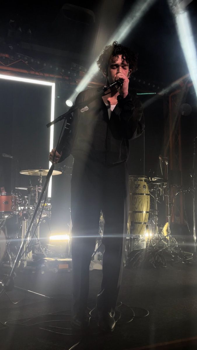 a man singing into a microphone while standing in front of two other men on stage