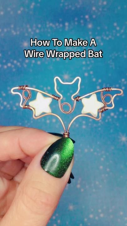 a hand holding a wire wrapped bat pin with green and white designs on it's back