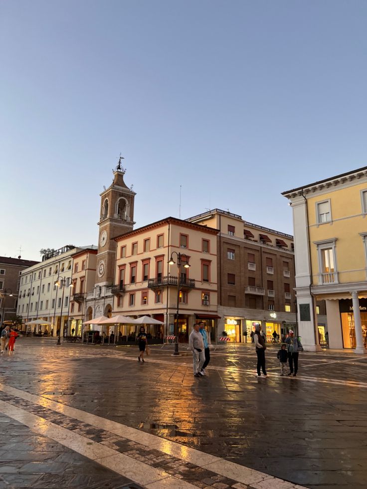 people are walking around in the middle of a city square at sunset or sunrise time