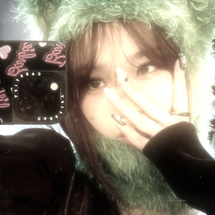 a girl wearing a furry green hat and holding her hand to her face with both hands