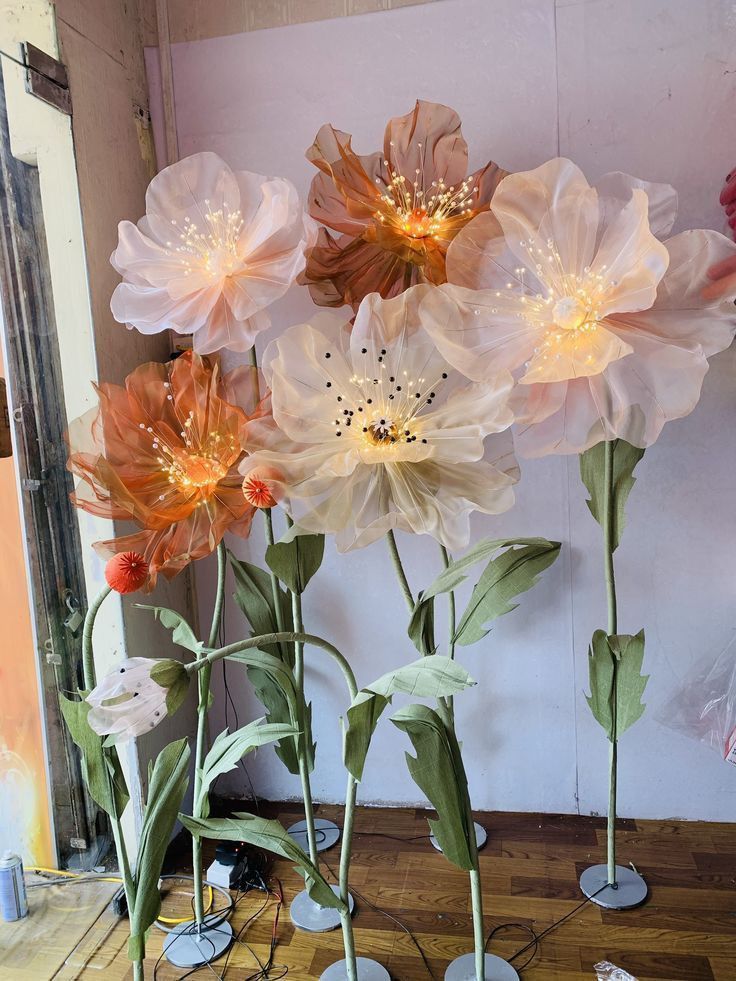 three vases filled with flowers sitting on top of a wooden floor next to a wall