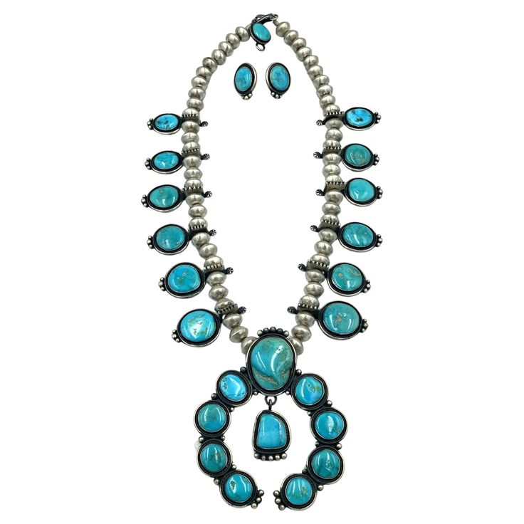 Sterling silver Navajo squash blossom necklace by award winning Navajo silversmith Tommy Jackson. The 27” necklace is comprised of 12 squash blossoms with a Blue Gem turquoise and a naja made up of 10 Blue Gem turquoise set in sterling silver. The sterling beads are handmade. Tommy is known for carefully selecting his stones and uses only the highest quality of turquoise and coral he can find. The Blue Gem mine, which is no longer active, produced a great variety of turquoise, from intense blue to deep green with an irregular matrix. The Blue Gem mine, which began production in 1934 yielded the most valuable Blue Gem turquoise because of its rich color and hardness. Award winning Navajo silversmith Tommy Jackson, is a third generation silversmith, following the footsteps of his parents, Ma Gem Mining, Squash Blossom, Squash Blossom Necklace, Navajo Jewelry, Blue Gems, Necklace Earring Set, Rich Color, Earring Set, Coral