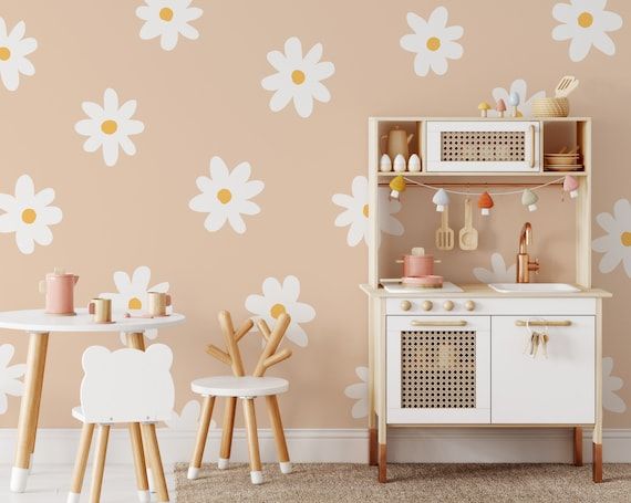 a child's play kitchen with white flowers on the wall and wooden stools