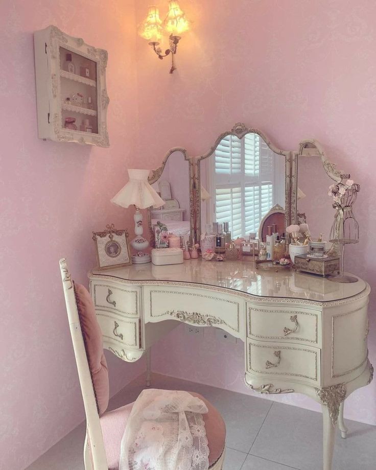 a white desk with a mirror and chair in front of it, next to a pink wall